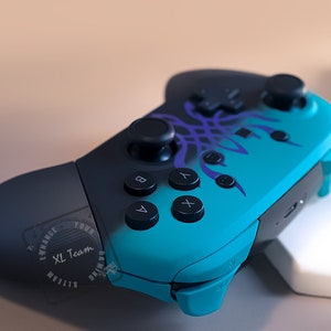 May include: A blue and black video game controller with a purple and black design. The controller has a circular button in the center and four buttons on the right side. The controller is on a white surface.