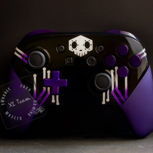 May include: A black and purple video game controller with a white skull design and a purple plus button. The controller has a purple and white circuit board design and the text "XL Team Gaming" on the side.