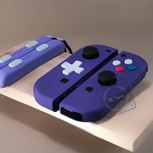 Puede incluir: Mandos Nintendo Switch Joy-Con de color morado y blanco con un bot&oacute;n m&aacute;s blanco y una pegatina en blanco y negro que dice "Enhance Your Game XL Team".
