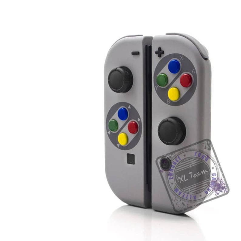 May include: A gray and white Nintendo Switch controller with a retro design. The controller has a black and white color scheme with a red, blue, green, and yellow button layout. The controller is in a closed position.