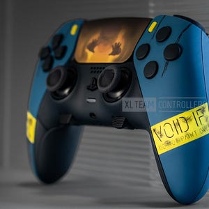 May include: A custom video game controller with a blue and black design. The controller features black buttons and joysticks, with yellow accents. The design includes an image of hands reaching out and the text "VOID IF DO NOT REMOVE PRINT CARE".