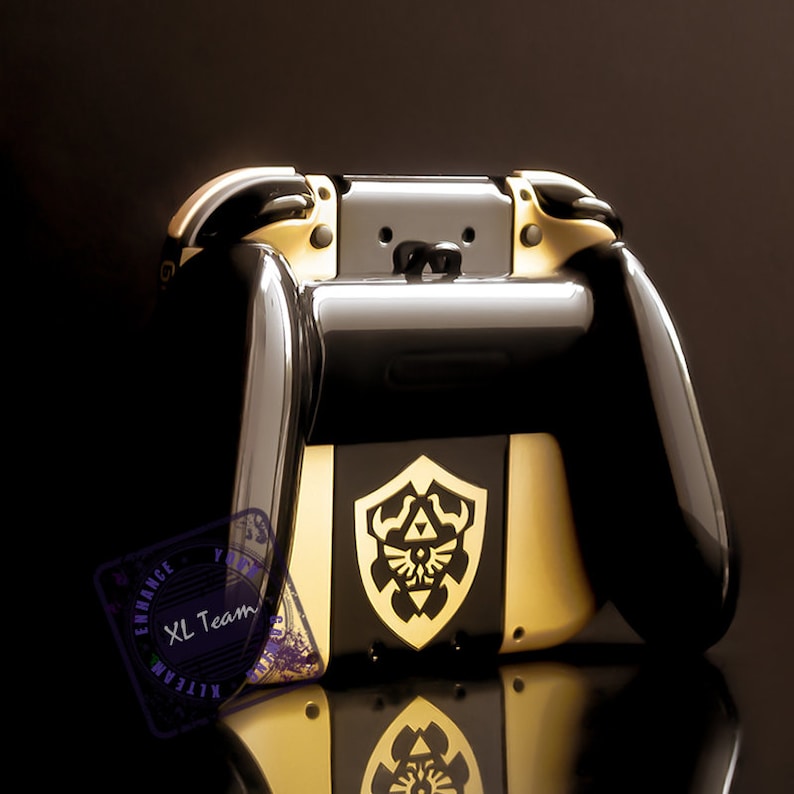 May include: A black and gold Nintendo Switch console with a custom design featuring the Triforce symbol from the Legend of Zelda video game series. The console has gold accents and a black and gold controller.