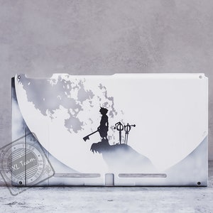 Op de afbeelding: Witte Nintendo Switch-console met een aangepast ontwerp met een silhouet van een personage dat een Keyblade vasthoudt tegen een witte en grijze achtergrond. Het ontwerp bevat de tekst "XL Team".