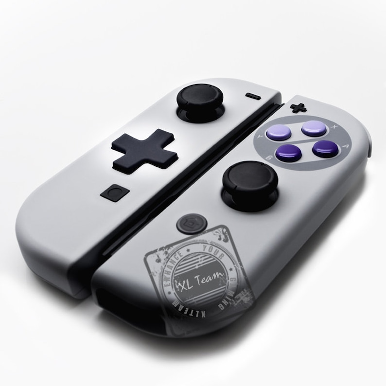 May include: A white and gray Nintendo Switch controller with a black cross button and a black and white sticker that says "Enhance Your XL Team Gaming".