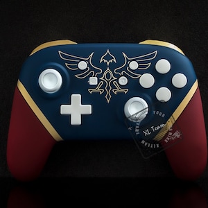 Könnte beinhalten: Ein benutzerdefinierter Nintendo Switch-Controller mit blauem und rotem Design. Der Controller verfügt über ein goldenes Emblem mit einem Vogel und dem Text "YOUR XL Team".