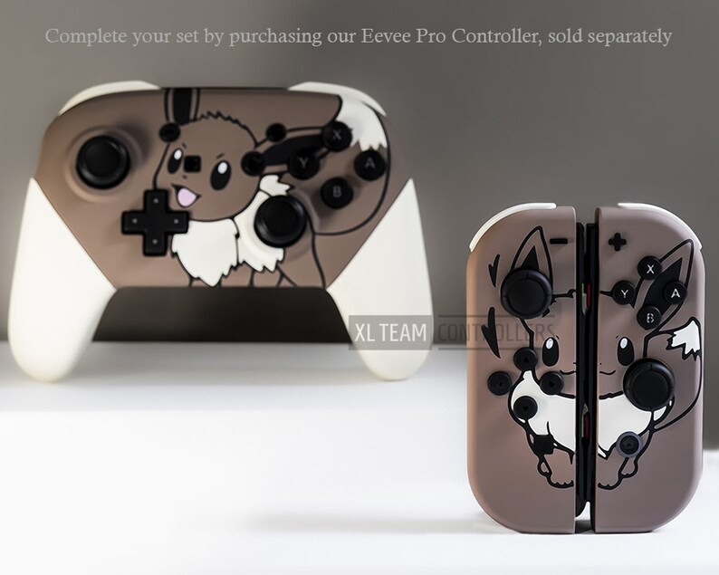May include: Two video game controllers with an Eevee design. One is a Pro Controller with white handles and a brown and white Eevee graphic. The other is a set of Joy-Cons with a similar design. The text "XL TEAM CONTROLLERS" is visible.