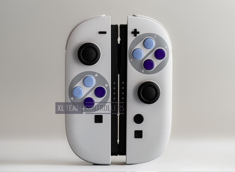 Puede incluir: Mando de juegos blanco con botones negros y de colores. El mando tiene un dise&ntilde;o retro con botones azules y morados. El texto "XL TEAM CONTROLLERS" es visible en la parte inferior izquierda.
