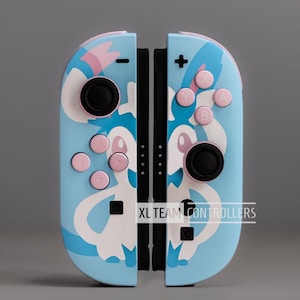 May include: A pair of light blue game controllers with a white and pink character design. The controllers have black joysticks and pink buttons. The text "XL TEAM CONTROLLERS" is visible on the bottom right of the controllers.