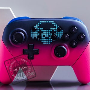 Könnte beinhalten: Ein rosa-blauer Nintendo Switch-Controller mit einem pixeligen Alien-Raumschiff-Design. Der Controller hat schwarze Tasten und ein schwarzes Steuerkreuz.