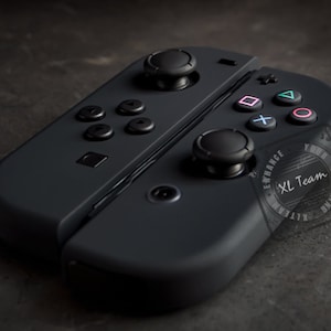 May include: A black Nintendo Switch controller with a custom design. The controller has a black and white logo that says "XL Team" and the words "Enhance Your Gaming".