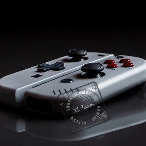 Könnte beinhalten: Ein weißer und grauer Gaming-Controller mit schwarzen und roten Knöpfen. Der Controller ist zusammengeklappt und hat einen schwarz-weißen Aufkleber auf der Unterseite mit der Aufschrift "XL Team Gaming".