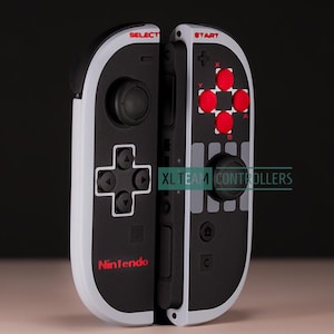 May include: Black and white Nintendo Switch Joy-Con controllers with red accents. The controllers have a retro design with the words "SELECT" and "START" in red. The Nintendo logo is also visible.