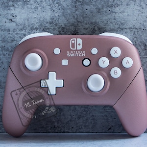 May include: A rose gold Nintendo Switch controller with white buttons and a white Nintendo Switch logo. The controller has a textured surface.