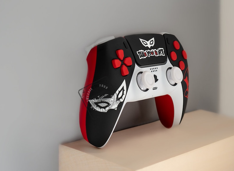 May include: A custom video game controller with a black, red, and white color scheme. The controller features a design with the text "TAKE YOUR HEART" and a stylized mask. The buttons are red, and the joysticks are white.