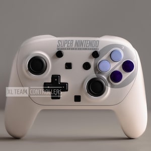 May include: A white wireless game controller featuring the text SUPER NINTENDO and XL TEAM CONTROLLERS. It includes two black analog sticks, a black directional pad, four action buttons in shades of light and dark purple, and black menu buttons.