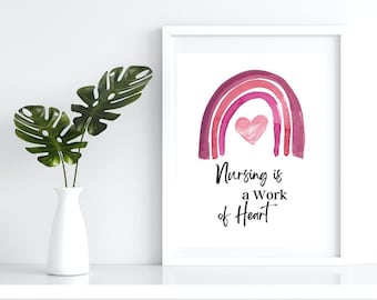 Könnte beinhalten: Ein weißer gerahmter Druck mit einem rosa Aquarell-Regenbogen und einem rosa Herzen in der Mitte. Der Text unter dem Regenbogen lautet: "Nursing is a work of heart."