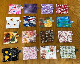 May include: A collection of small, square fabric coin purses with various patterns. Designs include floral, geometric, and novelty prints, such as sunflowers, a patriotic flag, and cartoon animals. Each purse has a snap closure and a small metal ring.