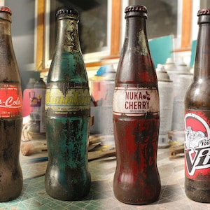 Puede incluir: Cuatro botellas de vidrio de estilo vintage con etiquetas envejecidas. Las botellas presentan diseños de Nuka-Cola, IronTide, Nuka Cherry y Vim. Las botellas tienen un aspecto envejecido, con tapas y etiquetas de color óxido.