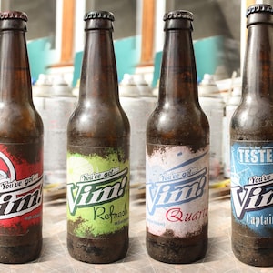 以下が含まれることがあります： 金属キャップが付いた4本の茶色のガラス瓶。各ボトルには「Vim！」の文字とその他のテキストが記載された異なるラベルが付いています。ラベルは赤、緑、青、白です。ボトルは木製の表面にあります。