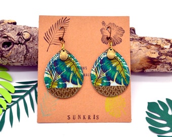 May include: A pair of teardrop-shaped earrings with a tropical leaf print. The earrings are made of metal and have a gold finish. The earrings are hanging on a brown card with the text "SUNKRIS" printed on it.