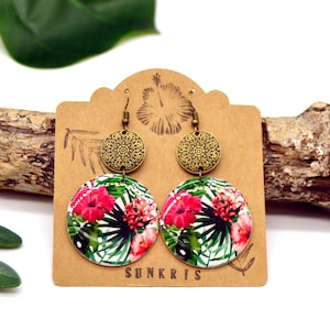 Peut inclure: Une paire de boucles d'oreilles rondes avec un motif floral tropical. Les boucles d'oreilles présentent un dessus de couleur laiton avec un motif de filigrane circulaire et un bas plus grand, circulaire, avec une impression vibrante de fleurs d'hibiscus rouges et de feuilles vertes.