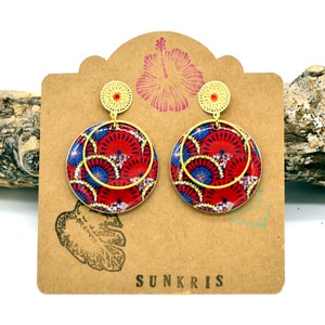 May include: Gold dangle earrings with a red, blue, and white patterned circle design. The earrings are displayed on a brown card with the word "SUNKRIS" printed on it.