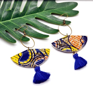 May include: A pair of colorful earrings with a blue, yellow, and orange patterned design. Each earring features a half-circle shape with a blue tassel hanging from the bottom.