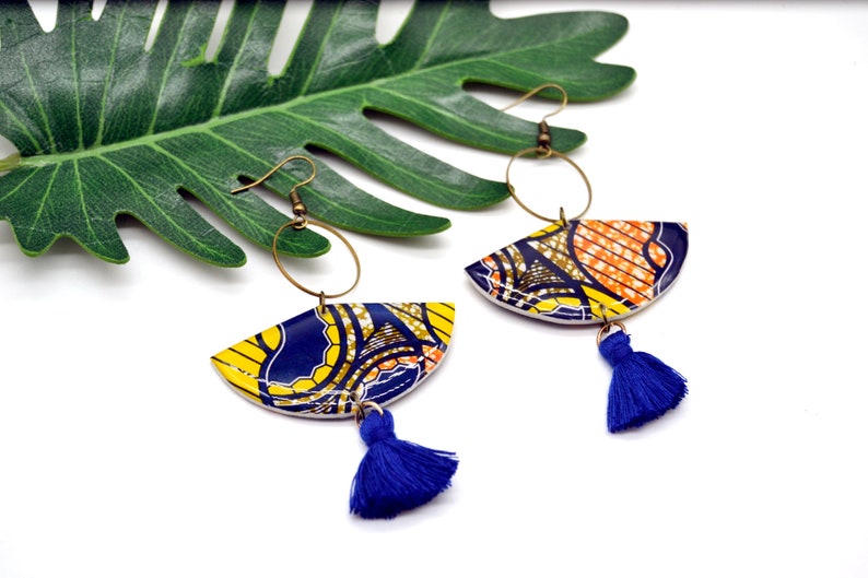 May include: A pair of colorful earrings with a blue, yellow, and orange patterned design. Each earring features a half-circle shape with a blue tassel hanging from the bottom.
