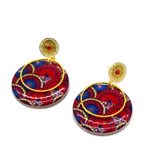 May include: A pair of red and blue patterned earrings with gold accents. The earrings are round and have a layered design.