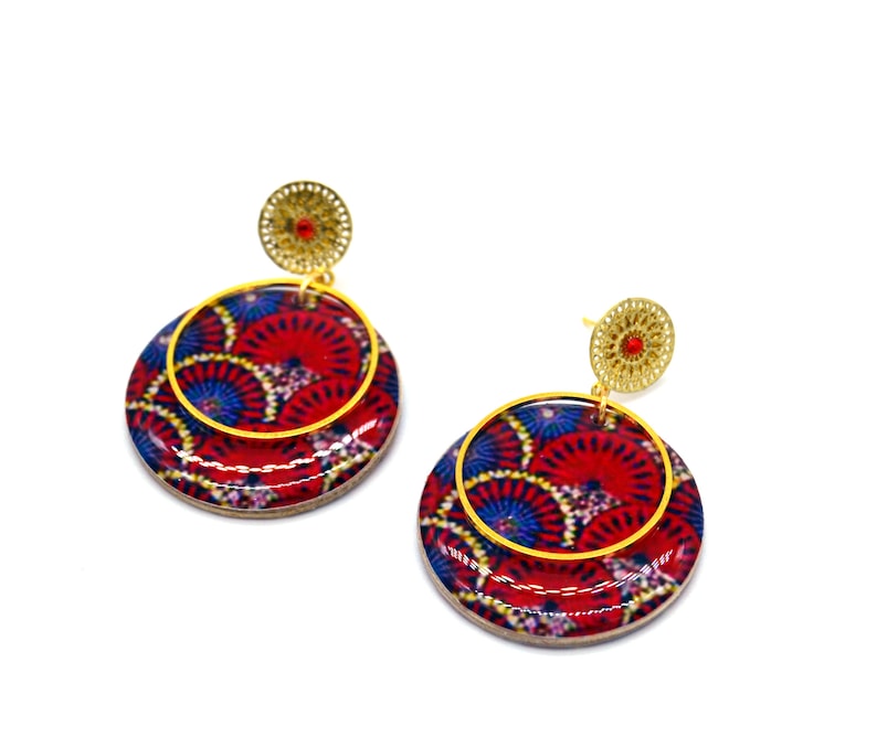 May include: A pair of red and blue patterned earrings with gold accents. The earrings are round and have a layered design.