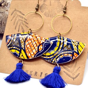 May include: A pair of blue and yellow patterned earrings with gold hoops and blue tassel accents. The earrings are on a brown card with the word "NKRIS" printed on it.
