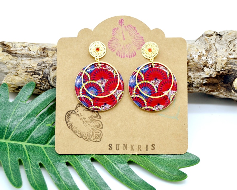 May include: A pair of gold hoop earrings with red and blue patterned circles. The earrings are on a brown card with the word "SUNKRIS" printed on it.