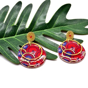 May include: A pair of red and blue patterned earrings with gold accents. The earrings are round and have a layered design.