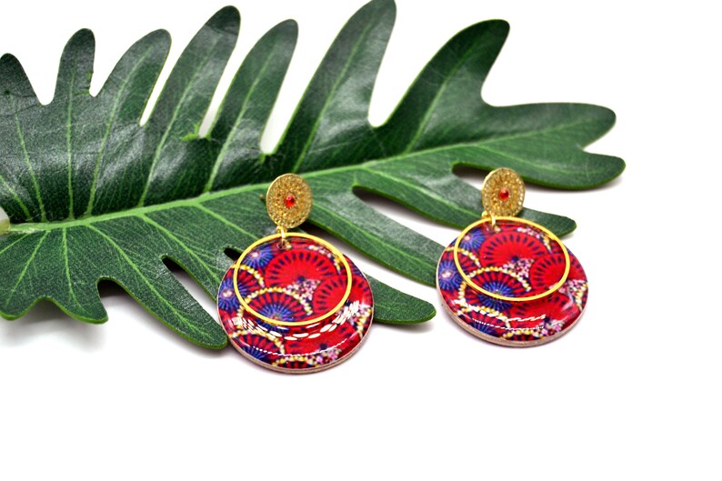 May include: A pair of red and blue patterned earrings with gold accents. The earrings are round and have a layered design.