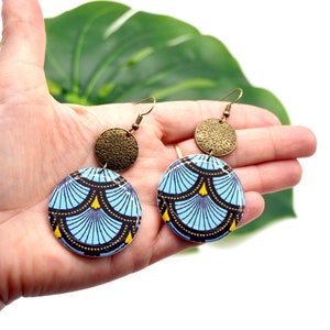 May include: A pair of blue and gold earrings with a geometric pattern. The earrings are made of wood and metal.