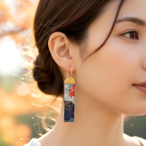 Gros plan d'une boucle d'oreille rectangulaire en papier japonais bleu foncé et rouge, motifs vagues et érable, suspendue à une attache dorée martelée.