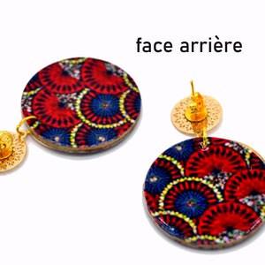 May include: A pair of gold tone earrings with round wooden discs featuring a colorful geometric pattern. The back of the earrings show the gold tone post and a circular back.