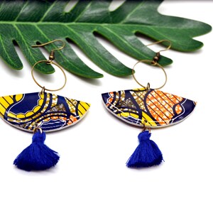 May include: A pair of colorful earrings with a blue tassel. The earrings are made of a patterned fabric with yellow, orange, and blue colors. The earrings are hanging from gold hoops.