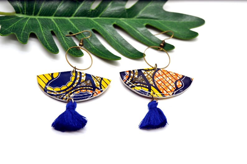 May include: A pair of colorful earrings with a blue tassel. The earrings are made of a patterned fabric with yellow, orange, and blue colors. The earrings are hanging from gold hoops.