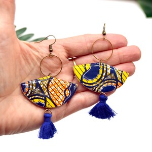 May include: A pair of colorful earrings with a blue tassel. The earrings are made of a yellow, orange, and blue patterned fabric and have a gold hoop.