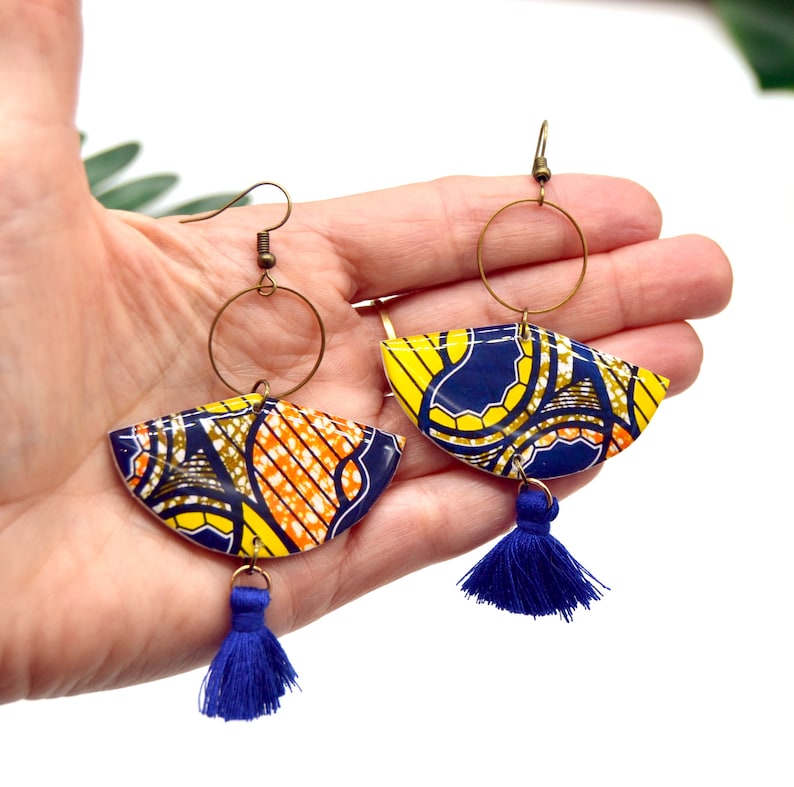 May include: A pair of colorful earrings with a blue tassel. The earrings are made of a yellow, orange, and blue patterned fabric and have a gold hoop.