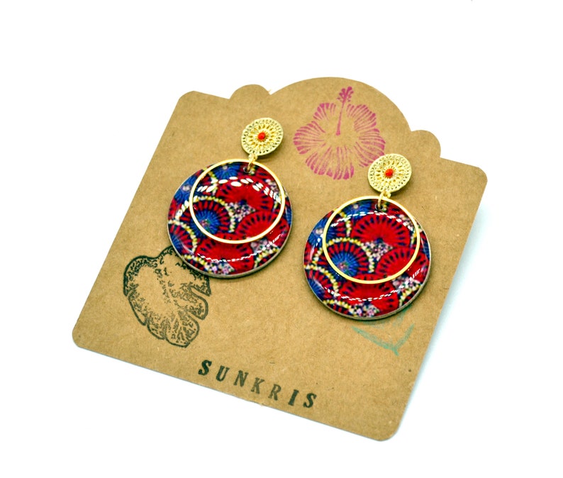 May include: A pair of gold hoop earrings with red and blue patterned circles. The earrings are on a brown card with the word "SUNKRIS" printed on it.