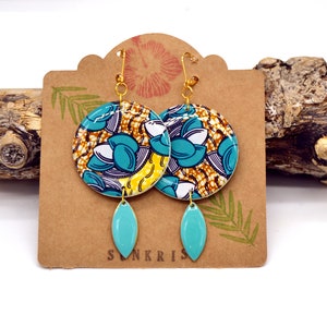 orecchini in resina di carta cerata con motivi di semi blu e bianchi su uno sfondo artigianale giallo e marrone