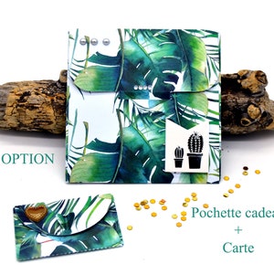 May include: A white gift bag with a tropical leaf pattern and a black cactus graphic. The bag is closed with a flap and has silver metal accents. The text "EN OPTION" is visible in the image. The bag is sitting on a piece of driftwood.