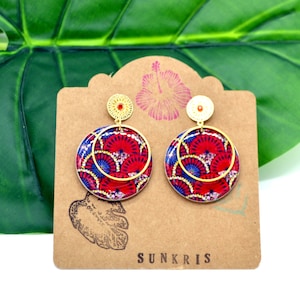May include: A pair of gold hoop earrings with red, blue, and white patterned circles. The earrings are on a brown card with the word "SUNKRIS" printed on it.