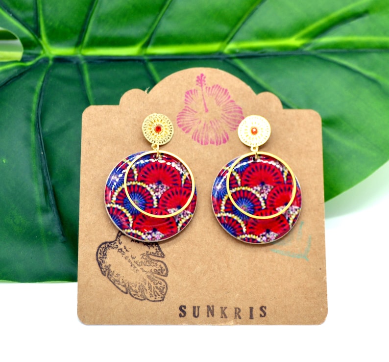 May include: A pair of gold hoop earrings with red, blue, and white patterned circles. The earrings are on a brown card with the word "SUNKRIS" printed on it.