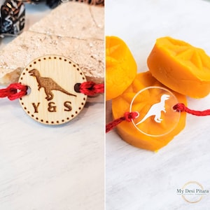May include: Two red string bracelets with a wooden charm and a clear plastic charm. Both charms feature a dinosaur design. The wooden charm has the letters Y & S engraved on it.