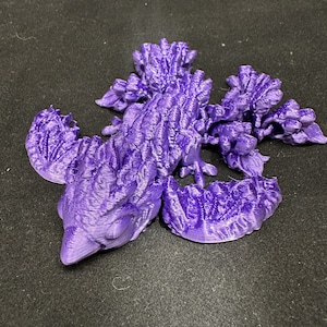 Puede incluir: Una figura de dragón impresa en 3D de color morado con detalles intrincados y una superficie texturizada.