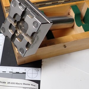 May include: A silver-colored precision tool with a cylindrical handle and a complex, multi-faceted head, resting in a wooden box with green felt padding. The box is open, revealing the tool and its storage. A quality certificate is visible.