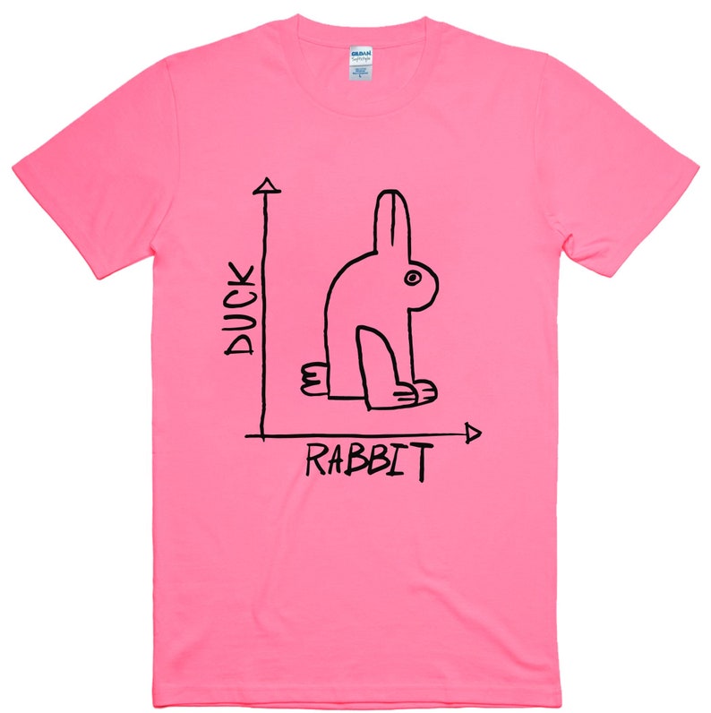 May include: A bright pink t-shirt with a black graphic of a rabbit, with the words "DUCK" and "RABBIT" in black text. The rabbit is drawn in a minimalist style, with a single eye and simple lines. The shirt is made of a soft material.